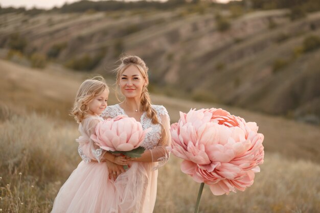 Mutter mit Tochter in rosa Märchenkleidern spazieren in der Natur. Die Kindheit der kleinen Prinzessin. Große rosa Zierblumen