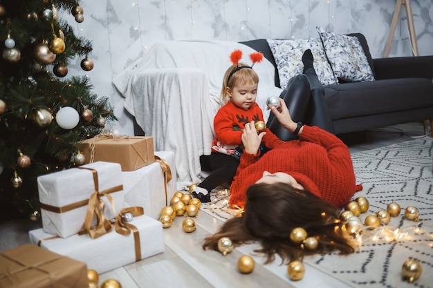Mutter mit Tochter in roten warmen Pullovern springen auf das Bett. Glückliche Mutterschaft. Warme familiäre Beziehungen. Weihnachten und Silvester Interieur. Liebe. Familienkonzept.