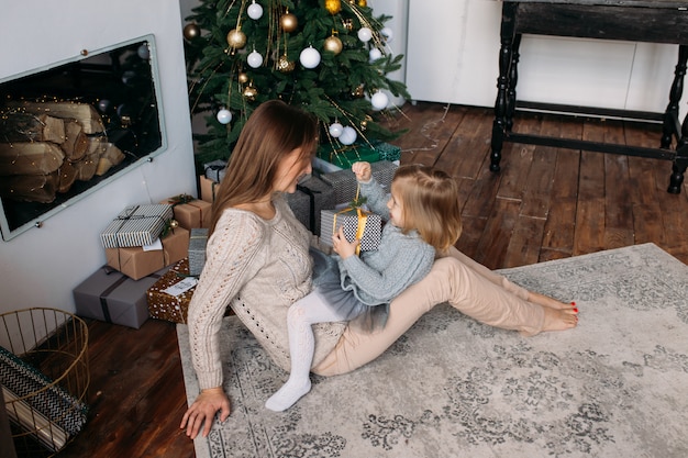 Mutter mit Tochter mit Geschenkbox nahe Weihnachtsbaum zu Hause.