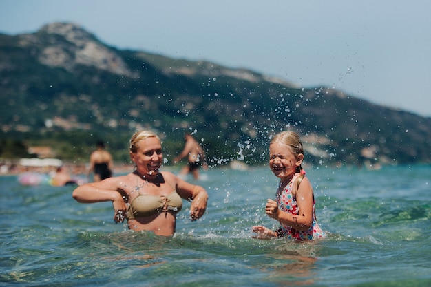 Mutter mit Tochter spielt im Wasser, schöne Badebekleidung, lacht und lächelt, Wasserspritzer.