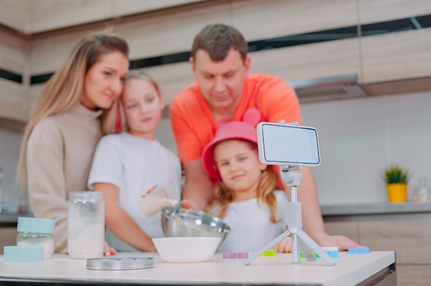 Mutter mit Vater bringt zwei Töchtern bei, in der Küche Teig zu kochen.