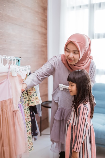 Mutter muslim, die zusammen ein Kleid für ihre Tochter im Bekleidungsgeschäft auswählt. Mama und Kind shoppen im Boutique-Shop