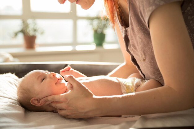 Mutter passt auf und hält ihr kleines Baby auf einem Bett liegend