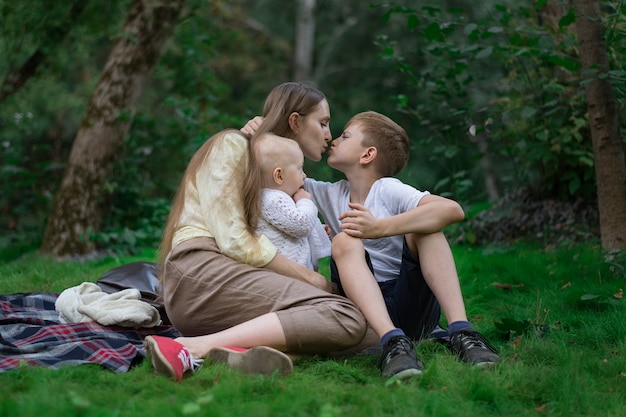 Mutter ruht mit zwei Kindern in der Natur. Familienpicknick im Park. Mama küsst Sohn