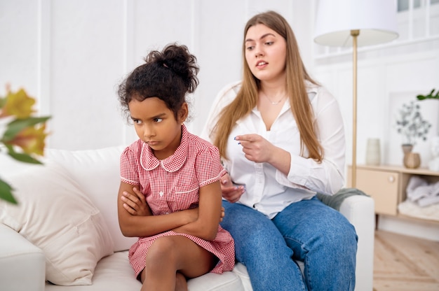 Mutter schimpft mit ihrer kleinen Tochter auf dem Sofa im Wohnzimmer