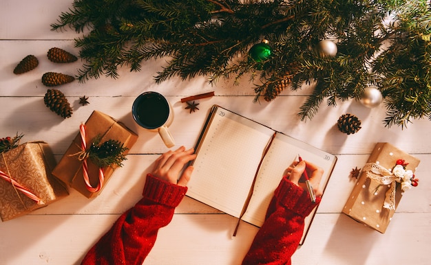 Mutter schreibt in Notizbuch und To-Do-Liste der Geschenke für Weihnachten und Neujahr