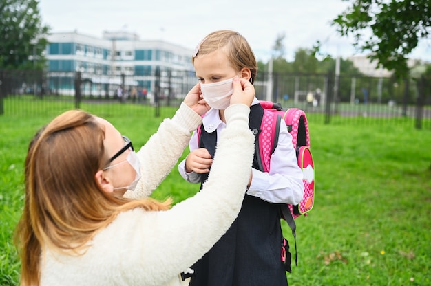 Mutter setzt eine Schutzmaske auf ihr Schulmädchen