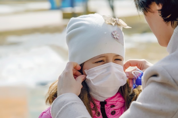 Mutter setzt für ihre Tochter eine medizinische Schutzmaske gegen das Virus auf, schützt das Kind mit einer medizinischen Maske gegen das Virus, schützt gegen das Coronavirus, covid-19