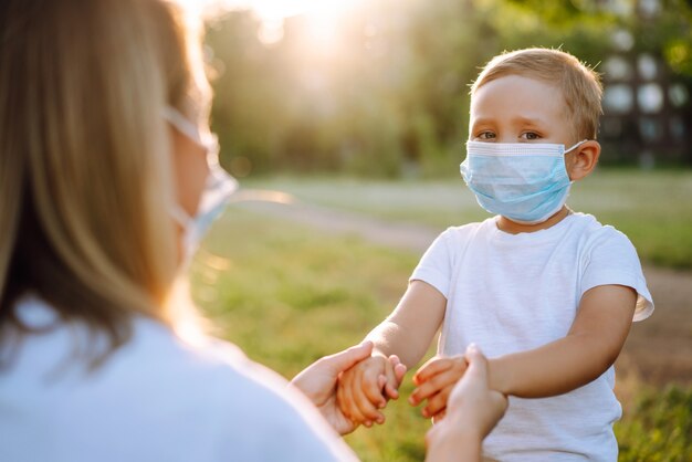 Mutter setzt im Park die sterile medizinische Maske des Kindes auf Covid2019