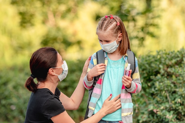 Mutter setzt Schutzmaske auf kleine Tochter, bevor sie zurück zur Schule geht