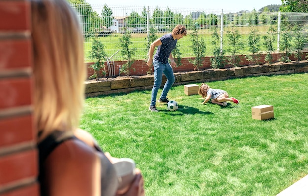 Mutter sieht ihrem Mann und ihrem Sohn beim Fußballspielen im Garten zu