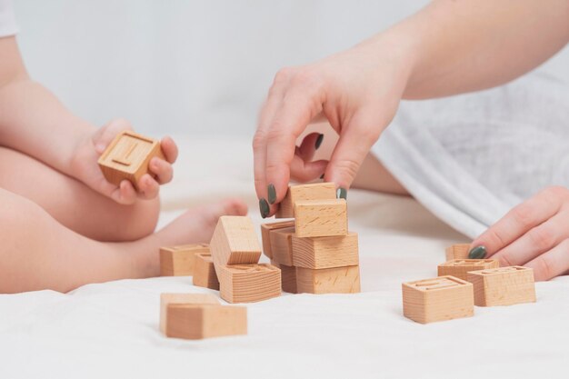 Mutter spielt mit einem Kind, das ein Haus aus umweltfreundlichen Holzwürfeln baut, Nahaufnahme Das Konzept der frühen kindlichen Entwicklung durch Spiele Gemütliche, gemütliche Atmosphäre Muttertag Kindertag