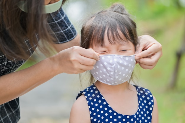 Mutter trägt eine stoffmaske für kleine mädchen, die vor coronavirus geschützt sind, wenn das kind das haus verlässt