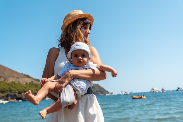 Mutter trägt einen Hut mit ihrem Baby in Cala Montjoi, Strand des Parc Natural del Cap Creus, Gerona, Costa Brava von Katalonien im Mittelmeer. Spanien