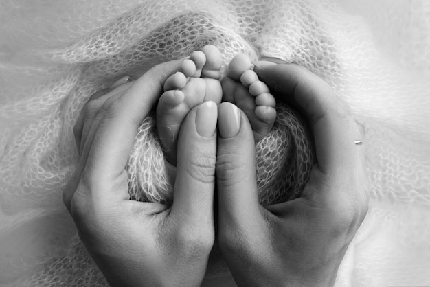 Mutter tut Massage auf ihrem Babyfuß Closeup Babyfüße in Mutterhänden Prävention der Entwicklung von Plattfüßen Muskeltonus Dysplasie Familienliebe Pflege Gesundheitskonzepte Schwarz-Weiß-Makro