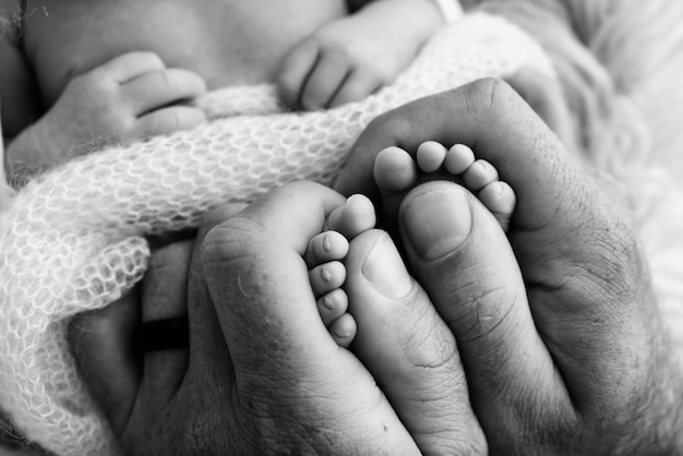 Mutter tut Massage auf ihrem Babyfuß Closeup Babyfüße in Mutterhänden Prävention der Entwicklung von Plattfüßen Muskeltonusdysplasie Familienliebe Pflege- und Gesundheitskonzepte Schwarz und Weiß