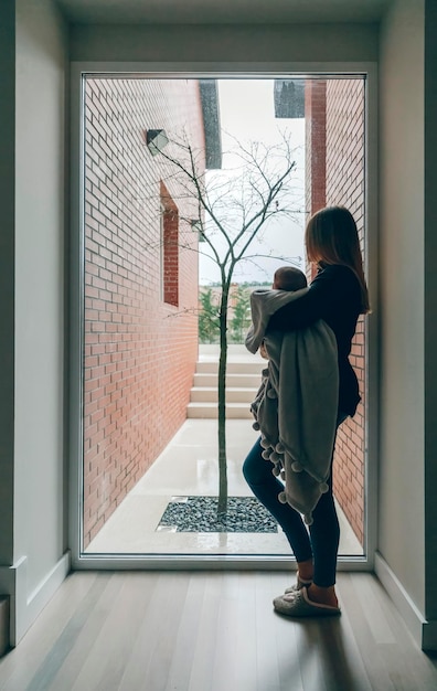 Mutter umarmt ihr Baby und schaut durch das Fenster