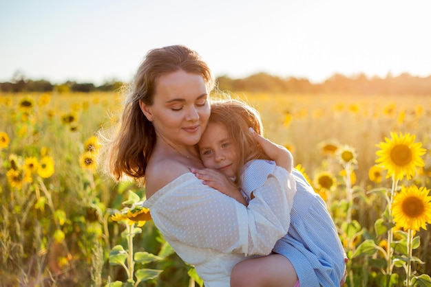 Mutter umarmt ihre kleine Tochter Eine schöne junge Frau mit einem 4-jährigen Kind im Arm in einem Sonnenblumenfeld Sommer