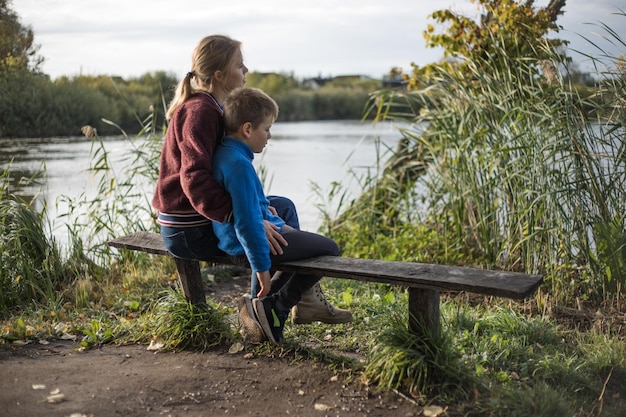 Mutter umarmt Junge im Freien auf der Bank Mutter küsst Sohn im Park Kostbare Momente zwischen Mutter und Sohn