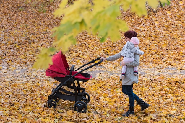 Foto mutter und baby, die mit kinderwagen im herbstlichen wald spazieren. mutter und süßes baby im herbstpark.