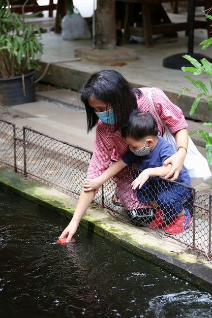 Mutter und Baby füttern Fische im Teich.