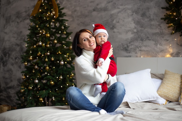 Mutter und Baby in rotem Hut Sankt lächeln mit Weihnachtsbäumen innerhalb des Hauses
