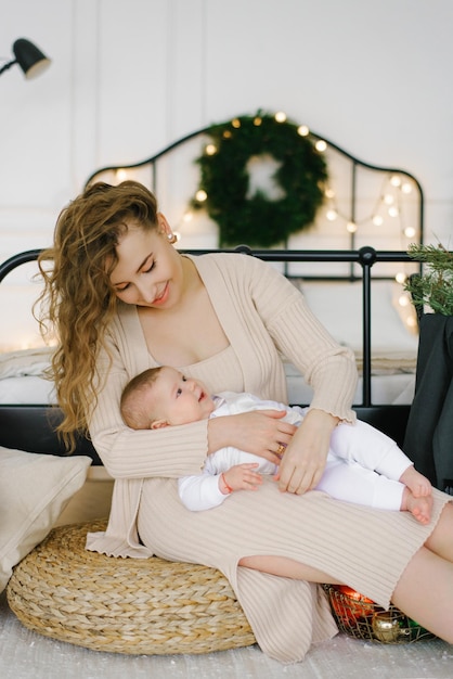 Mutter und Baby kuscheln auf dem Hintergrund eines Bettes und eines Weihnachtsbaums