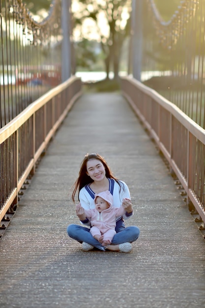 Mutter und Baby sitzen bei Sonnenuntergang auf der Brücke