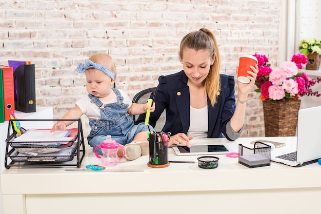 Mutter und Geschäftsfrau, die zu Hause mit Laptop-Computer arbeiten und mit ihrem Baby spielen.