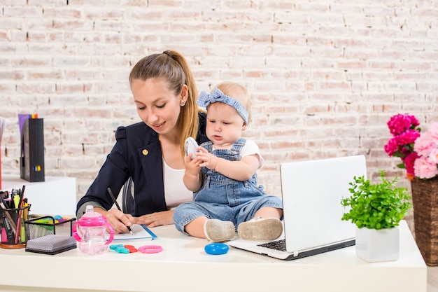 Mutter und Geschäftsfrau, die zu Hause mit Laptop-Computer arbeiten und mit ihrem Baby spielen.