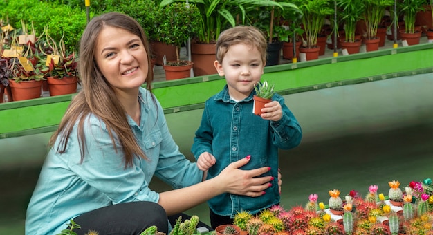 Mutter und ihr Baby in einem Pflanzenladen, der Kakteen betrachtet. Gartenarbeit im Gewächshaus. Botanischer Garten, Blumenanbau, Konzept der Gartenbauindustrie