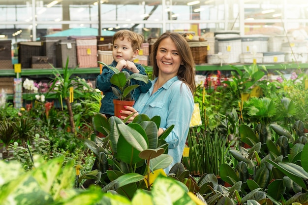 Mutter und ihr Baby wählen in einem Pflanzengeschäft Pflanzen aus. Gartenarbeit im Gewächshaus. Botanischer Garten, Blumenanbau, Konzept der Gartenbauindustrie