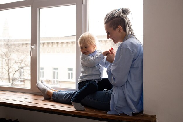 Mutter und ihr kleiner Sohn sitzen auf der Schwelle in der Nähe des Fensters