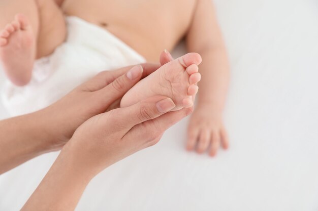 Mutter und ihr süßes Kind auf weißem Bett Nahaufnahme Babymassage und Übungen