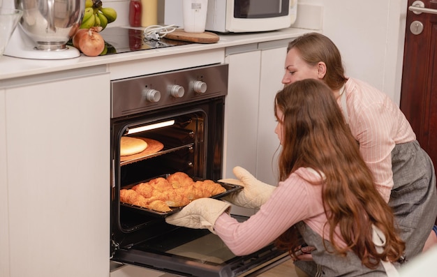 Mutter und ihre jüngere Tochter in einem modernen Küchenbereich feiern freudiges Lernen backen Kuchendekoration glückliche kleine Tochter bereiten am Wochenende zu Hause süßes Gebäck mit fürsorglicher Mutter zu