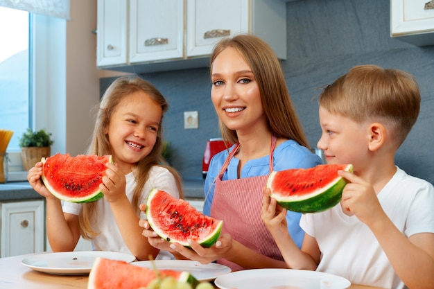 Mutter und ihre Kinder essen Wassermelone in ihrer Küche