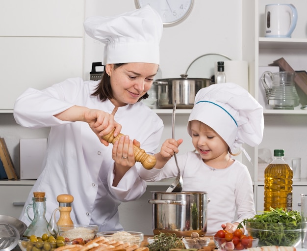 Mutter und ihre kleine Tochter in Uniform salzen die Suppe zusammen