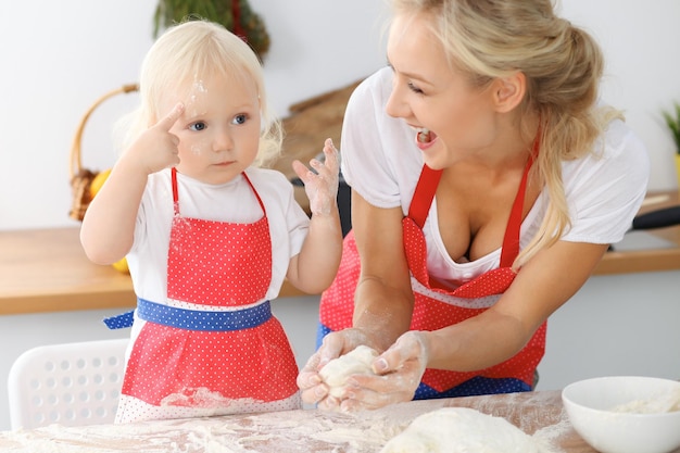 Mutter und ihre kleine Tochter kochen Feiertagstorte oder Plätzchen für den Muttertag. Konzept der glücklichen Familie in der Küche.