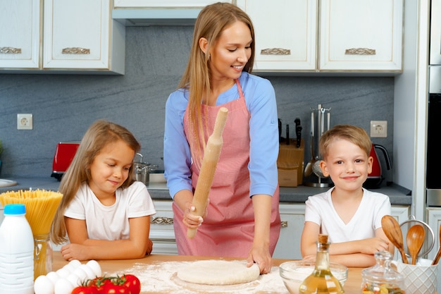Mutter und ihre kleinen Kinder, Jungen und Mädchen, helfen ihr, Teig zuzubereiten