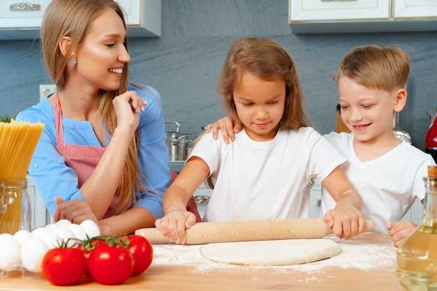 Mutter und ihre kleinen Kinder, Jungen und Mädchen, helfen ihr, Teig zuzubereiten