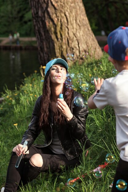 Mutter und jugendlich Sohn auf grünem Rasen mit Seifenblasen im öffentlichen Frühlingspark, die sich an sonnigen Tagen amüsieren