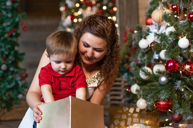 Mutter und Junge unter Weihnachtsbaum mit Geschenken. Frau mit Kind zum neuen Jahr