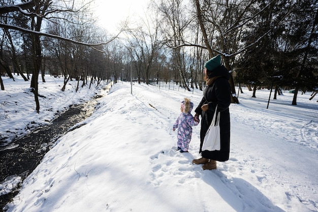 Mutter und Kind an einem sonnigen, frostigen Wintertag im Park füttern Enten auf dem zugefrorenen Fluss