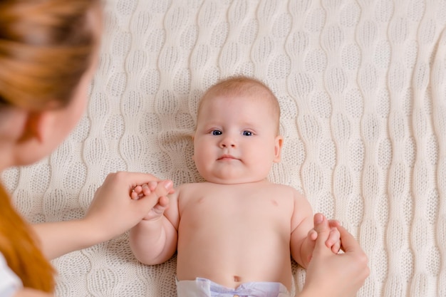 Mutter und Kind auf einem weißen Bett Mutter und Baby in Windel spielen im sonnigen Schlafzimmer