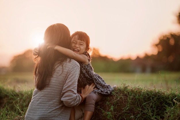 Mutter und Kind, die unter dem Sonnenunterganghimmel umarmen