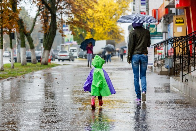 Mutter und Kind gehen mit einem Regenschirm im Regen in die Stadt