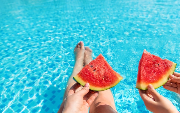 Mutter und Kind halten Wassermelonenstücke am Pool