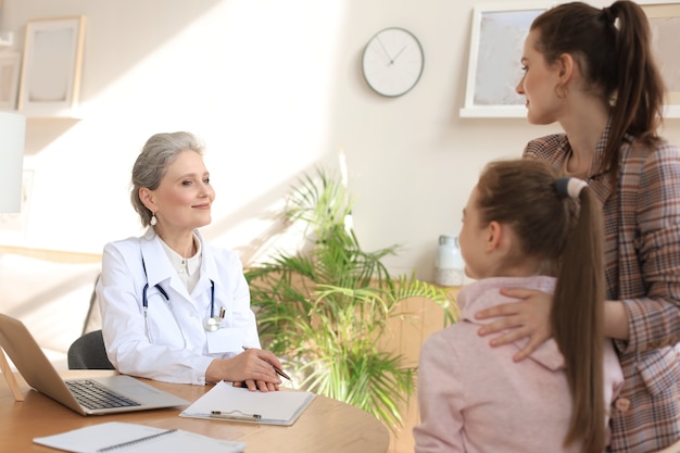 Mutter und Kind in der Arztpraxis treffen den Kinderarzt, sie sitzen am Schreibtisch im Krankenhaus.