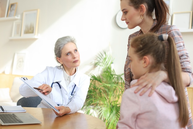 Mutter und Kind in der Arztpraxis treffen den Kinderarzt, sie sitzen am Schreibtisch im Krankenhaus.