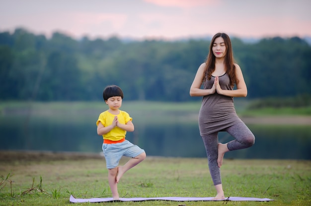 Mutter und Kind machen Yoga-Übungen auf Gras im Park vor Sonnenuntergang im Sommer.